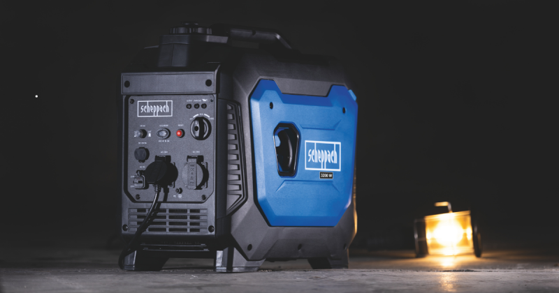 Niebiesko-czarny agregat prądotwórczy marki Scheppach pracujący w ciemnym pomieszczeniu, z podłączonym przewodem zasilającym lampę w tle.